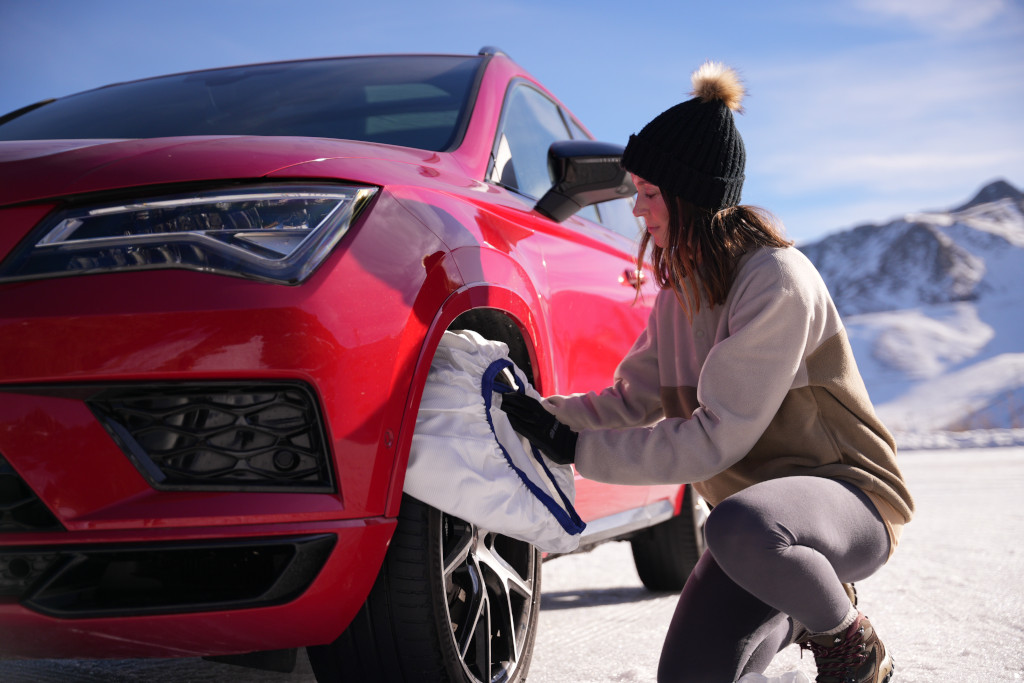 Mujer preparando una funda de nieve junto a un vehículo rojo en un entorno nevado.