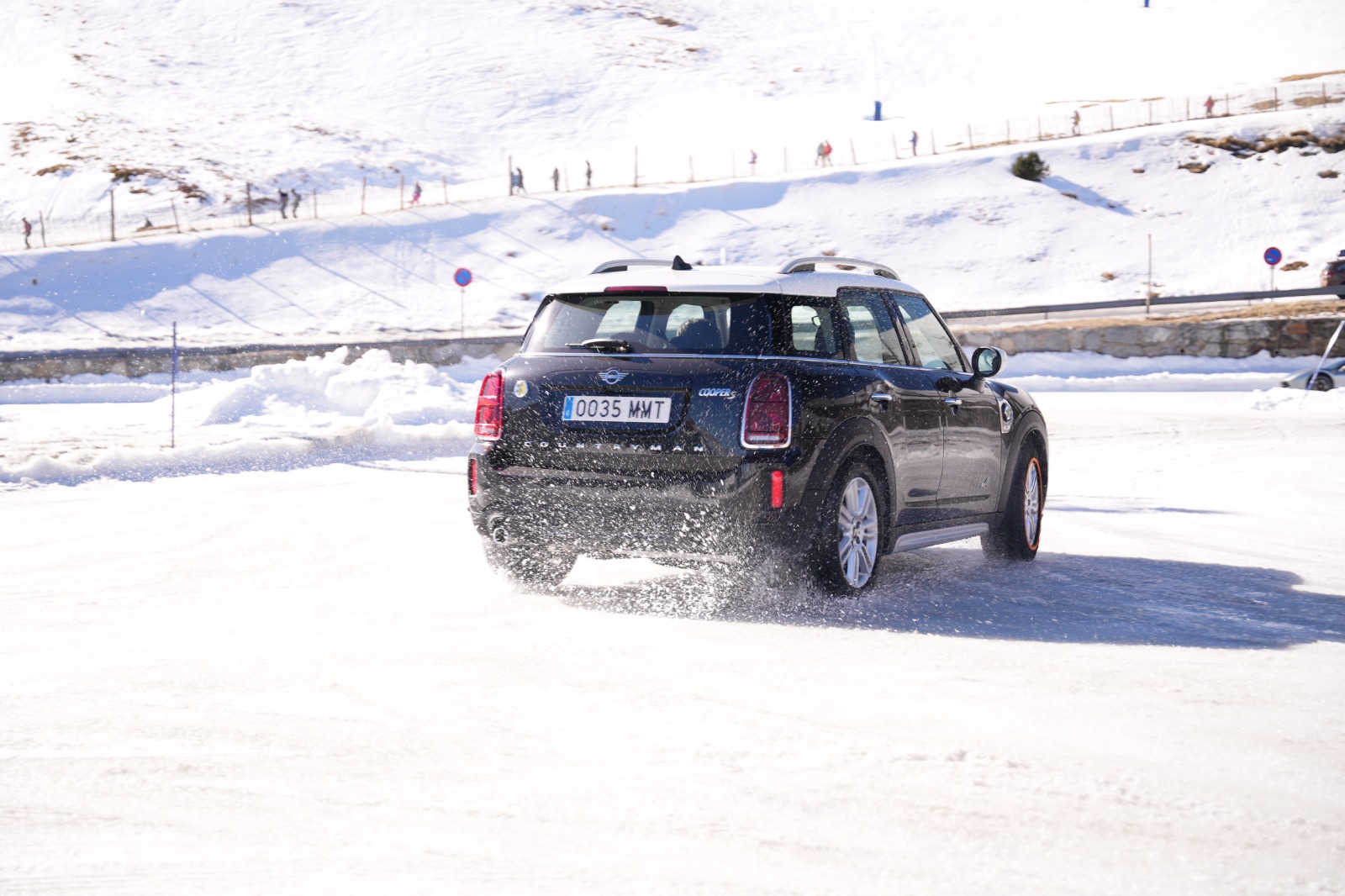 Un Mini Cooper negro conduciendo sobre una superficie nevada en un entorno montañoso.