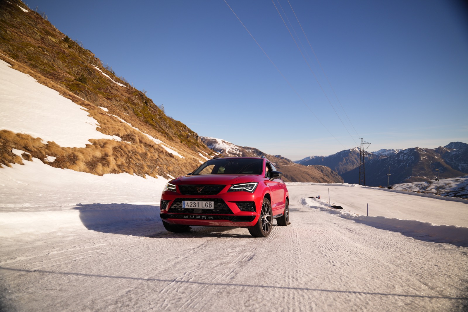 Un SUV Cupra rojo conduciendo sobre una carretera parcialmente cubierta de nieve en un entorno montañoso.