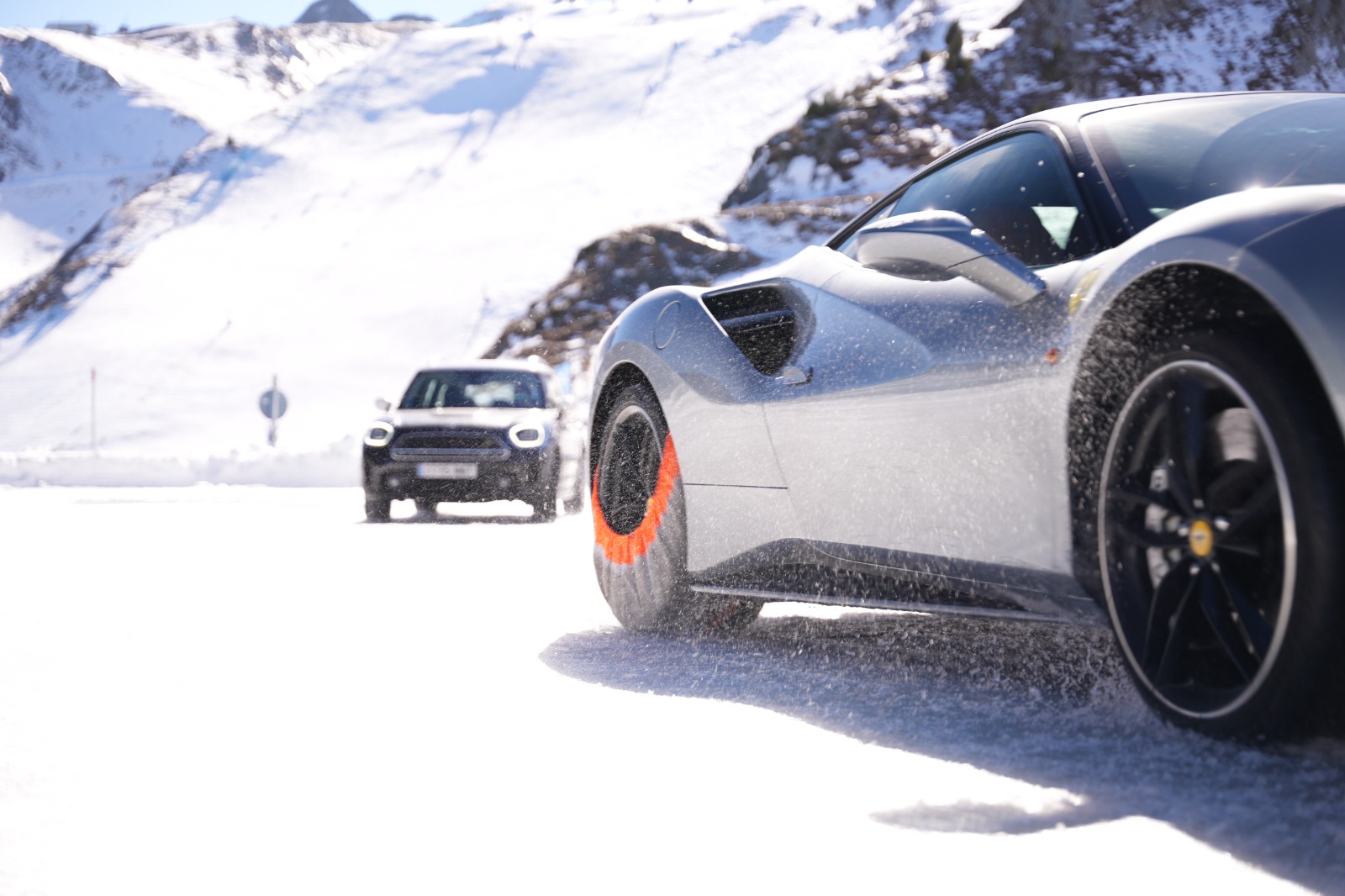 Coche deportivo con fundas de nieve naranjas y un SUV al fondo en un entorno nevado.