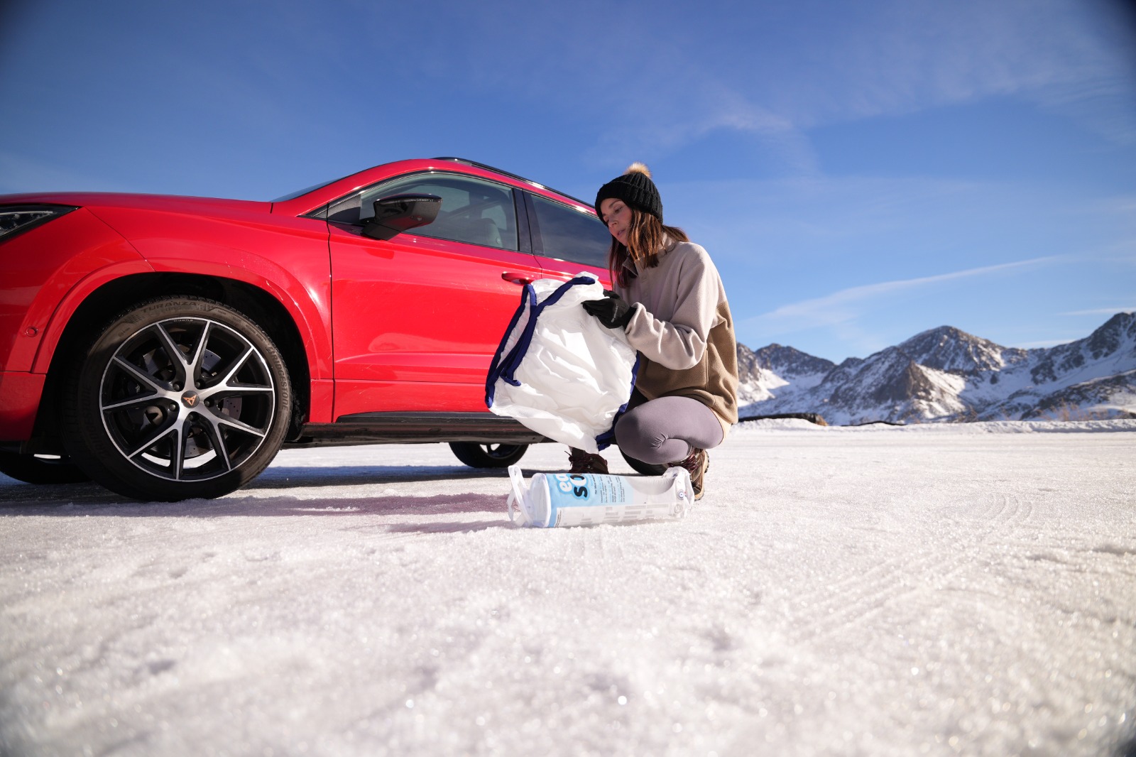 Mujer preparando una funda de nieve junto a un vehículo rojo en un entorno nevado.