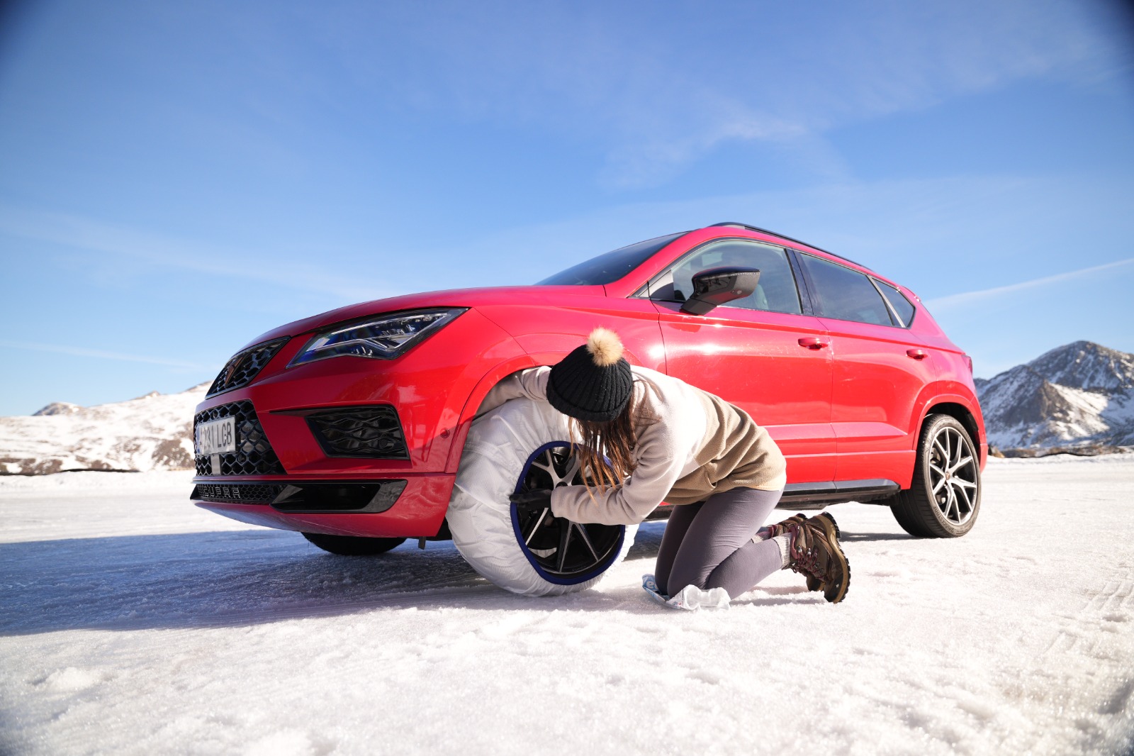 Mujer preparando una funda de nieve junto a un vehículo rojo en un entorno nevado.