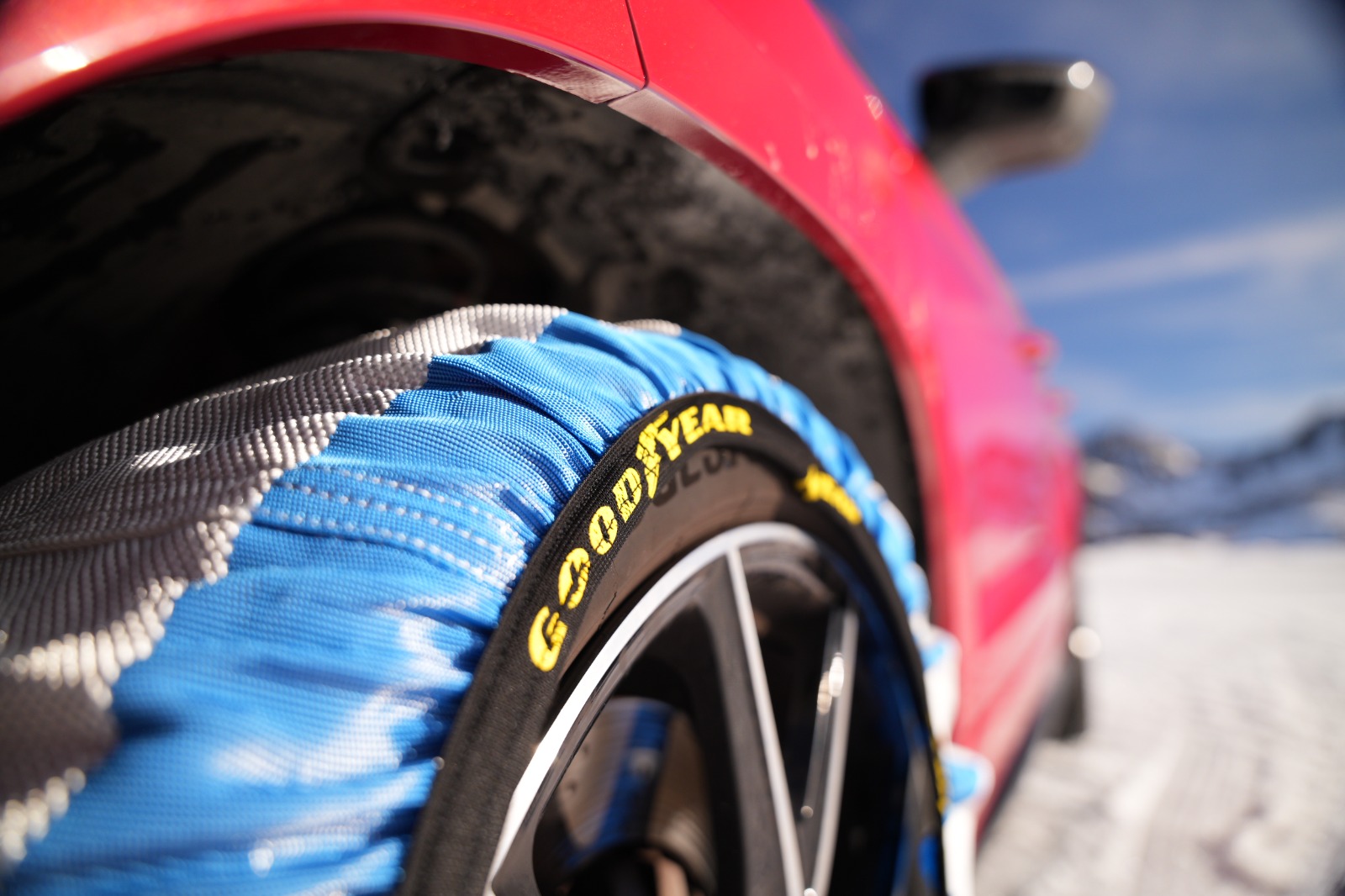 Primer plano de una funda de nieve Goodyear en color azul instalada en la rueda de un coche rojo.