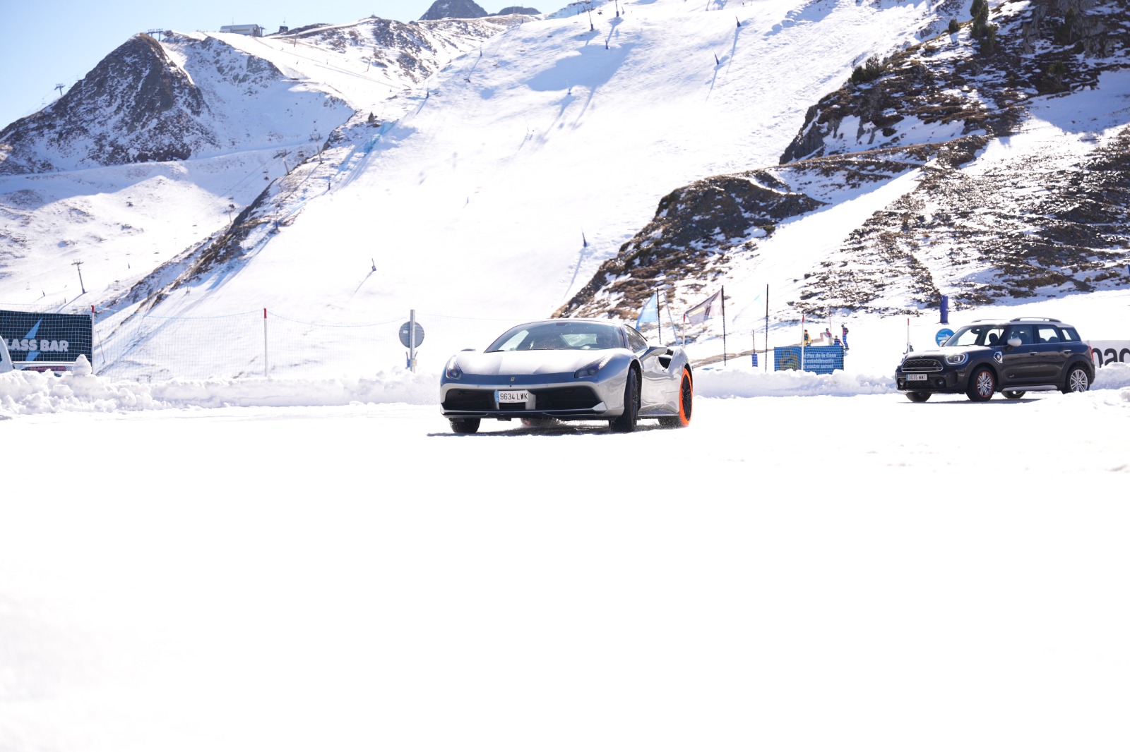 Coche deportivo gris y SUV negro en un entorno nevado de montaña.