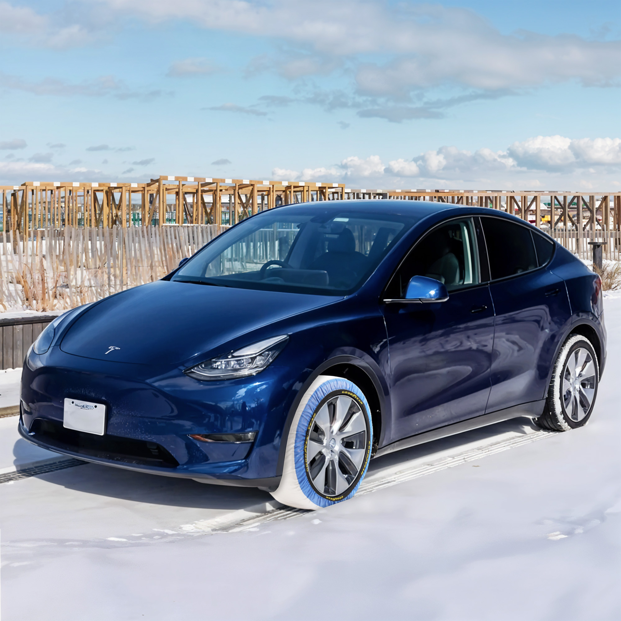 Tesla Model Y azul equipado con fundas de nieve Goodyear en sus ruedas, estacionado sobre nieve.